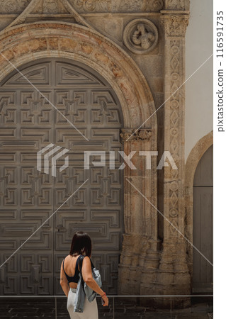 A woman by a large door, near medieval architecture and brickwork A woman by a large door, near medieval architecture and brickwork 116591735