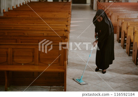 High angle view long shot of young African American Catholic nun wiping floor at nave in cathedral, copy space 116592184
