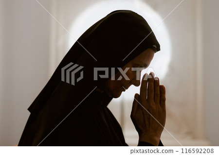 Side view backlight closeup of devout senior Caucasian Catholic nun praying to God,copy space Side view backlight closeup of devout senior Caucasian Catholic nun praying to God,copy space 116592208