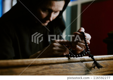 Medium closeup shot of senior Caucasian nun holding beads in hands sitting on pew in church and praying to God 116592277
