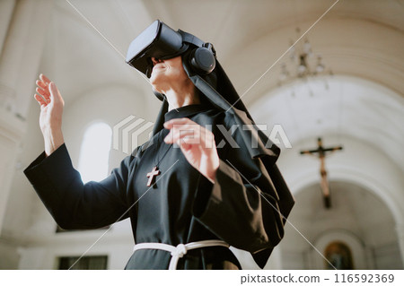 Low angle view medium shot of senior Caucasian nun standing inside Catholic cathedral building using VR technologies for education 116592369