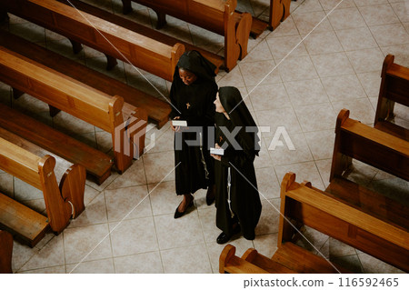 High angle view of two ethnically diverse young and mature Catholic nuns walking along nave and having conversation High angle view of two ethnically diverse young and mature Catholic nuns walking along nave and having conversation 116592465