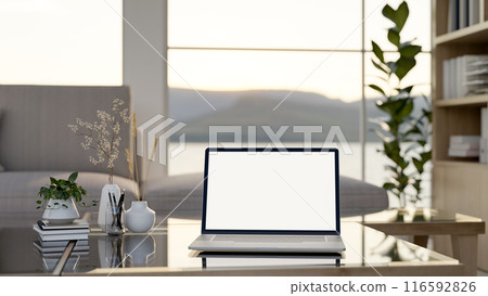 A laptop computer mockup and accessories on a coffee table in a modern bright living room. 116592826