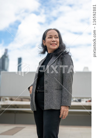 A confident, happy Asian senior businesswoman stands in the big urban city, looking at the sky. A confident, happy Asian senior businesswoman stands in the big urban city, looking at the sky. 116592881