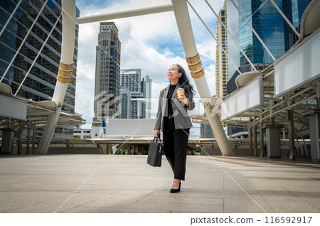 A successful mature Asian businesswoman walking in the city with her takeaway coffee and a briefcase A successful mature Asian businesswoman walking in the city with her takeaway coffee and a briefcase 116592917