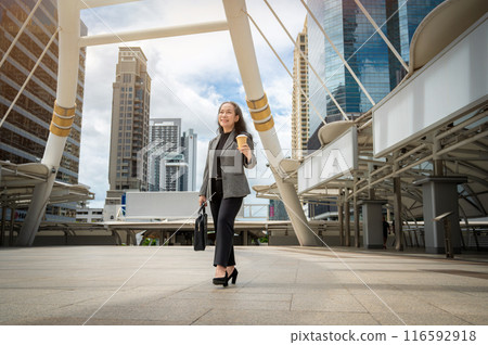 A confident, happy mature Asian businesswoman is commuting to work, walking in the city. 116592918