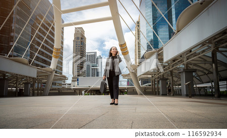 A professional mature Asian businesswoman is talking on the phone while walking in the urban city. 116592934