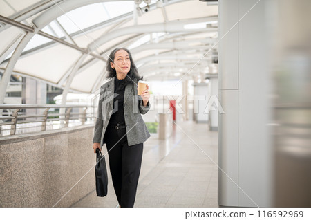 Confident mature Asian businesswoman is commuting to work, walking on the skywalk in the urban city. Confident mature Asian businesswoman is commuting to work, walking on the skywalk in the urban city. 116592969