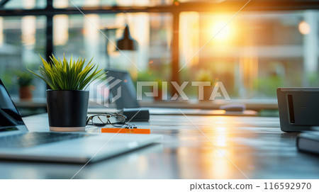 Blurred focus of modern office desk with laptop, plant, glasses. Abstract office interior background Blurred focus of modern office desk with laptop, plant, glasses. Abstract office interior background 116592970