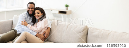 Happy Loving Family. Beautiful african american man and woman cuddling and relaxing on the couch at home in living room, smiling couple looking at camera and posing, copy space 116593910