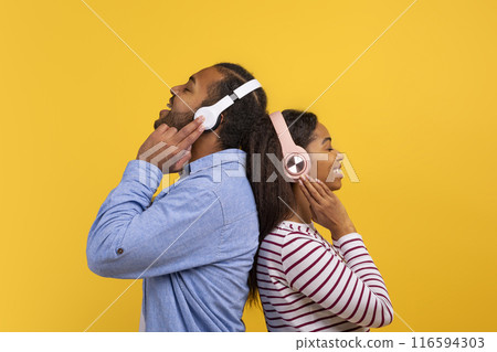 African American man and woman are shown wearing headphones, listening to music. They appear focused on their music, possibly enjoying the sound quality. 116594303