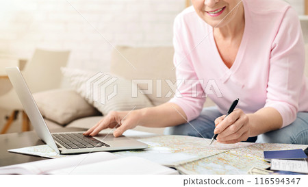 Cropped of senior woman is seated on couch, engaged in work on a laptop with focused concentration. Her hands are tapping on the keyboard as she looks at the screen intently Cropped of senior woman is seated on couch, engaged in work on a laptop with focused concentration. Her hands are tapping on the keyboard as she looks at the screen intently 116594347