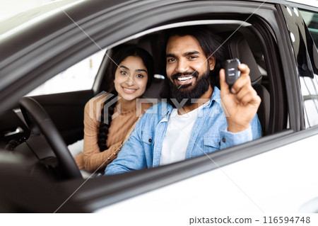 A cheerful and excited Indian couple is seated inside a new car. The man, with a beard, holds up car keys, indicating they have likely just purchased the vehicle, while the woman smiles warmly A cheerful and excited Indian couple is seated inside a new car. The man, with a beard, holds up car keys, indicating they have likely just purchased the vehicle, while the woman smiles warmly 116594748