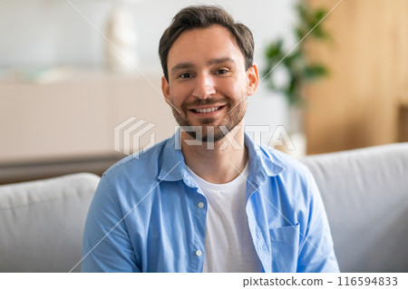 A man with a cheerful expression is seated on a sofa, displaying a bright smile. He appears comfortable and content as he relaxes while sitting on the furniture. A man with a cheerful expression is seated on a sofa, displaying a bright smile. He appears comfortable and content as he relaxes while sitting on the furniture. 116594833