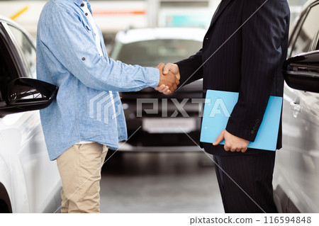 Cropped of two individuals are standing in front of a car, engaged in a handshake gesture. Both men are dressed formally, and the car in the background adds a professional touch to the scene. Cropped of two individuals are standing in front of a car, engaged in a handshake gesture. Both men are dressed formally, and the car in the background adds a professional touch to the scene. 116594848