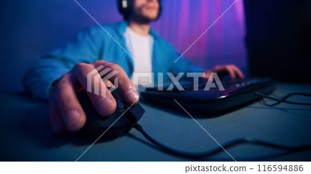 A close-up image of a gamers hand using a computer mouse while playing a game on their desktop. The focus is on the hand and the mouse, cropped 116594886