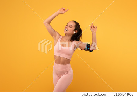 A young woman with a beaming smile is captured mid-dance against a bright yellow backdrop, dressed in form-fitting athletic wear, and is clearly reveling in a moment of triumph or celebration A young woman with a beaming smile is captured mid-dance against a bright yellow backdrop, dressed in form-fitting athletic wear, and is clearly reveling in a moment of triumph or celebration 116594903