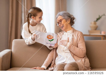 An older woman and a young girl are seated on a couch. The woman appears to be engaged in conversation with the girl, who is listening attentively An older woman and a young girl are seated on a couch. The woman appears to be engaged in conversation with the girl, who is listening attentively 116595026