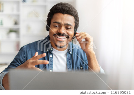 A young African American man with a warm smile is participating in a lively conversation over a video call. He wears a casual denim shirt and effortlessly communicates using his hand gestures A young African American man with a warm smile is participating in a lively conversation over a video call. He wears a casual denim shirt and effortlessly communicates using his hand gestures 116595081