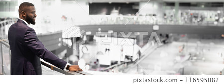 Cheerful african american young businessman looking down at his office, satisfied with results of his business, modern business center interior, panorama with copy space, back view 116595082