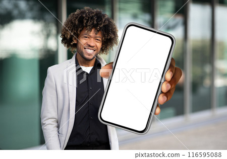 African American man is standing while holding a cell phone in his hand, looking at the screen. He appears focused and engaged with the device, possibly texting or browsing. African American man is standing while holding a cell phone in his hand, looking at the screen. He appears focused and engaged with the device, possibly texting or browsing. 116595088