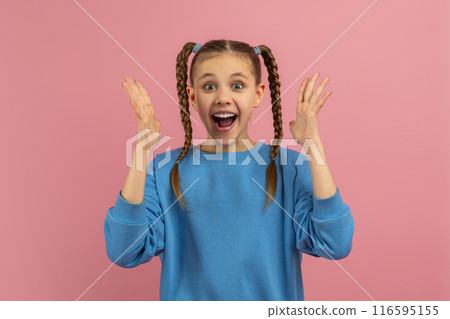 A young girl wearing a bright blue sweater stands against a vibrant pink backdrop, her hands raised in a gesture of surprise and elation 116595155