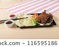 A traditional Asian dish, crispy duck is served with rice sheets, vegetables and dipping sauces on a wooden table, with a stripe towel in the background 116595186