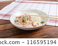 A white plate with Thai chicken curry and jasmine rice served on a wooden table with chopsticks resting on a checkered napkin 116595194