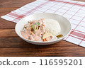 A savory meal presented with creamy chicken and vegetables next to a scoop of white rice on a wooden surface with a checkered napkin 116595201