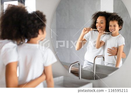 Black mother and her young child stand in front of a bathroom mirror as they both engage in their morning dental hygiene routine. Black mother and her young child stand in front of a bathroom mirror as they both engage in their morning dental hygiene routine. 116595211