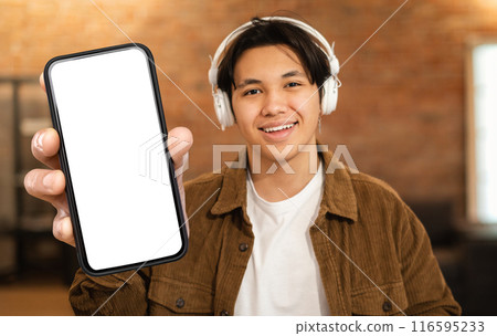 A man with headphones on holding a cell phone up in front of his face. He appears focused on the screen, possibly listening to music or engaging in a phone call. A man with headphones on holding a cell phone up in front of his face. He appears focused on the screen, possibly listening to music or engaging in a phone call. 116595233