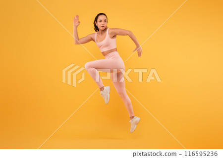 A woman wearing a pink outfit is captured mid-air as she jumps energetically. Her arms are outstretched and her legs are bent, showcasing a moment of dynamic movement and joy. A woman wearing a pink outfit is captured mid-air as she jumps energetically. Her arms are outstretched and her legs are bent, showcasing a moment of dynamic movement and joy. 116595236