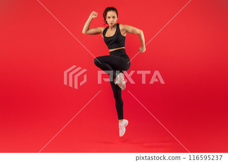 A fitness instructor is captured mid-motion while performing a high-knee exercise, showcasing her strength and agility. She is dressed in athletic wear and appears focused and determined 116595237