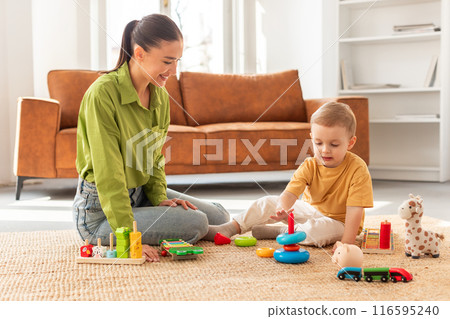 A woman is sitting on the floor, engaging with a child by playing together. They seem to be enjoying each others company in a cozy indoor setting. 116595240