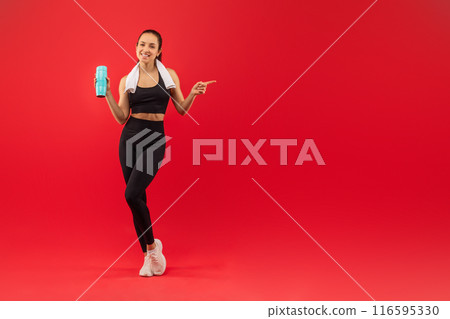 A smiling woman in black athletic wear, including leggings and a sports bra. She is holding a turquoise water bottle and has a white towel draped over her other arm, copy space A smiling woman in black athletic wear, including leggings and a sports bra. She is holding a turquoise water bottle and has a white towel draped over her other arm, copy space 116595330