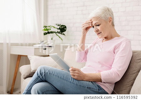 Confused senior woman using tablet computer, looking disappointed, doesn't understand modern gadgets, empty space 116595392