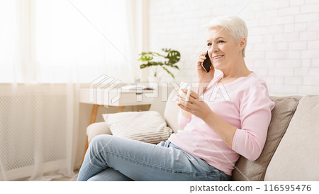 Cheerful senior lady having phone call on her smartphone and gossiping, enjoying fresh tea, free space 116595476