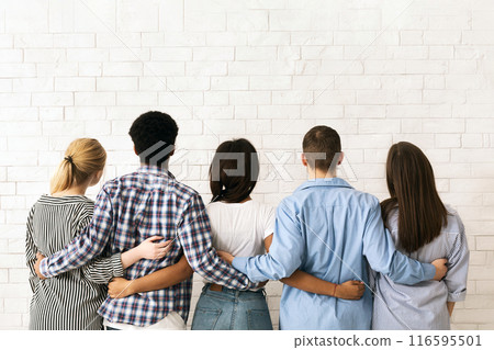 A group of multiethnic teenagers stands close together with their backs to the viewer, arms around each other in a display of friendship and unity, back view 116595501