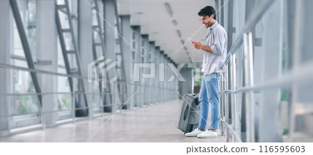 Texting he is fine. Smiling man with luggage messaging through his mobile phone, arriving to airport, empty space Texting he is fine. Smiling man with luggage messaging through his mobile phone, arriving to airport, empty space 116595603