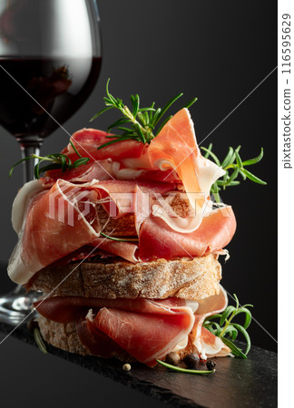 Ciabatta with prosciutto, rosemary and glass of red wine. Ciabatta with prosciutto, rosemary and glass of red wine. 116595629