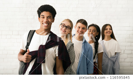 Five cheerful teenagers, three girls and two boys, are seen lined up against a white brick wall background. The group appears to be friends 116595845