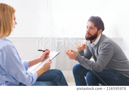 Handsome young man sitting on couch and talking to psychologist, doctor making notes, panorama with empty space Handsome young man sitting on couch and talking to psychologist, doctor making notes, panorama with empty space 116595978