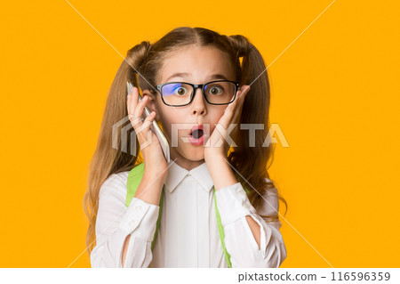 OMG, Mobile Phone Addiction. Shocked Little School Girl Holding Smartphone To Ear On Yellow Studio Background. Empty Space 116596359