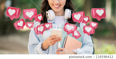Cropped of young woman is standing in a park, smiling as she looks at her phone. Around her are several bright pink hearts with white centers, representing social media likes Cropped of young woman is standing in a park, smiling as she looks at her phone. Around her are several bright pink hearts with white centers, representing social media likes 116596412