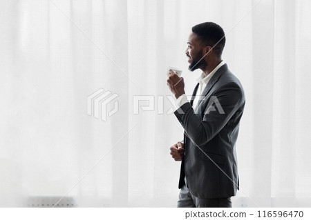 Cheerful african american businessman drinking coffee near window in office excited after successful deal, copy space 116596470