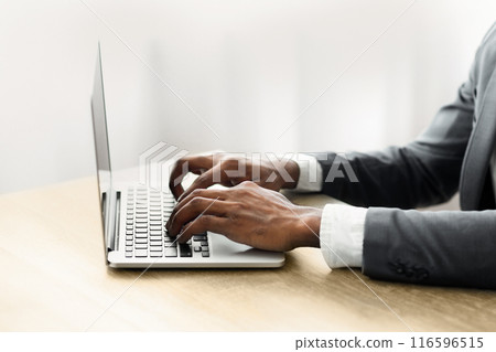 A businessman types on a laptop while sitting at a desk. 116596515