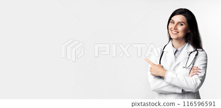 A smiling female doctor in a white coat points to the right with her right hand. Her arms are crossed and she is wearing a stethoscope. A smiling female doctor in a white coat points to the right with her right hand. Her arms are crossed and she is wearing a stethoscope. 116596591