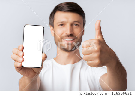 A man with a beard smiles and holds a smartphone with a blank screen while giving a thumbs up. A man with a beard smiles and holds a smartphone with a blank screen while giving a thumbs up. 116596651