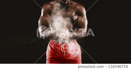 A muscular man claps his hands together, creating a cloud of white powder against a black background. A muscular man claps his hands together, creating a cloud of white powder against a black background. 116596758