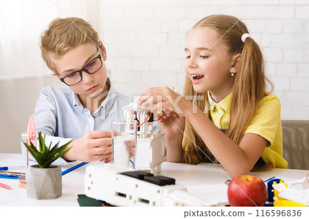 Two students, a boy and a girl, work together on a science project in a classroom setting. The boy is wearing glasses and is focused on robot 116596836